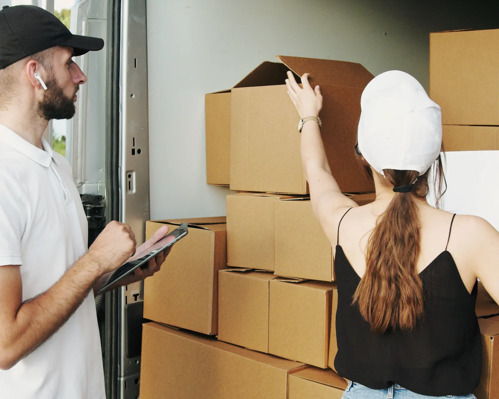 Two people checking packages and paperwork at the open rear of a vehicle.