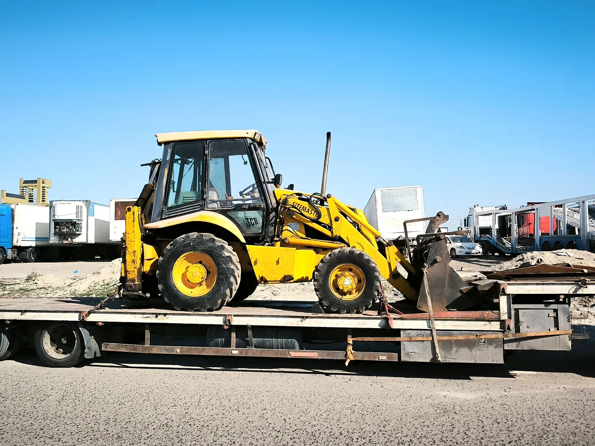 A yellow backhoe loader secured on a flatbed trailer.