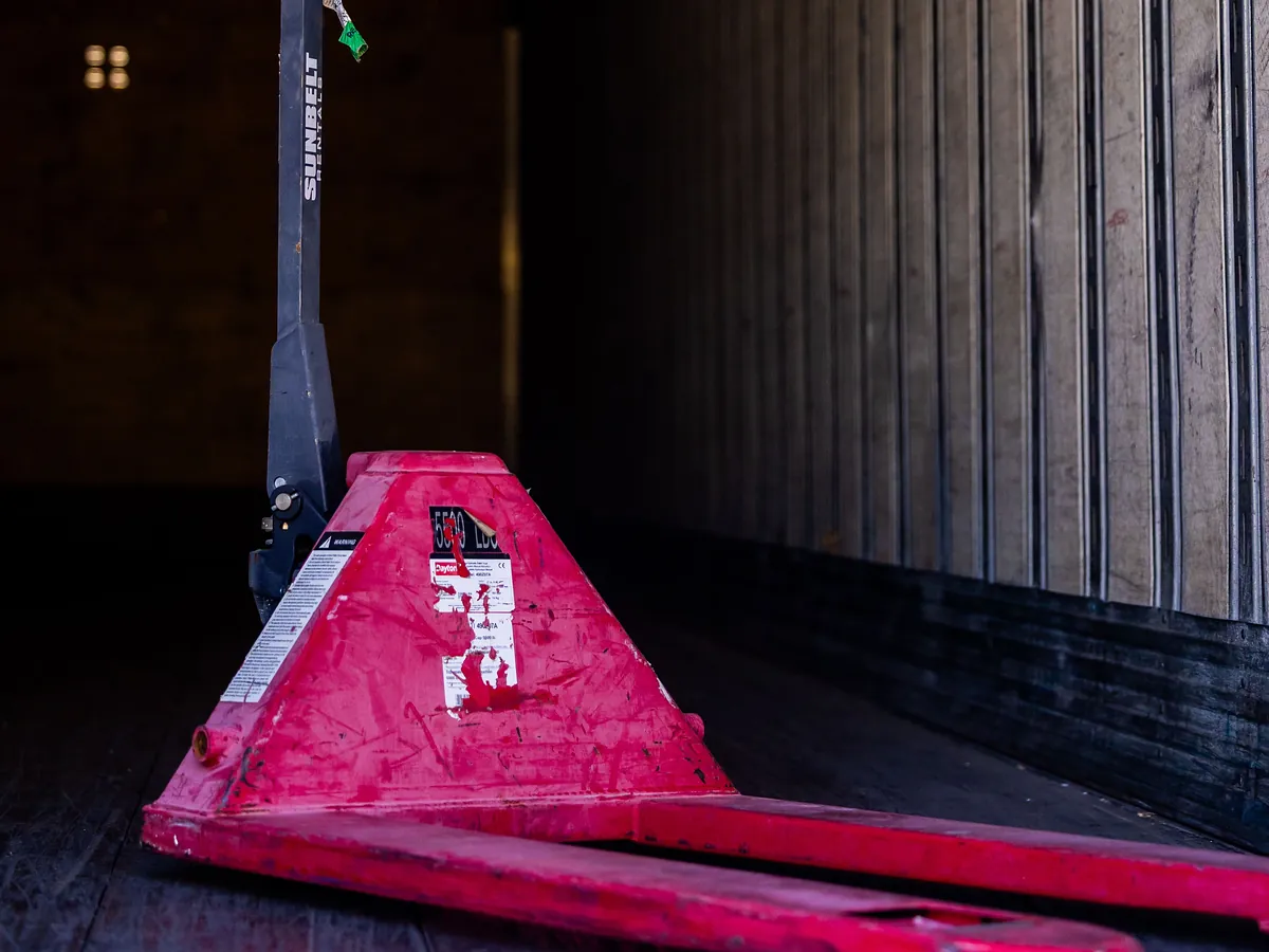 A red pallet jack resting inside the empty trailer of a truck.