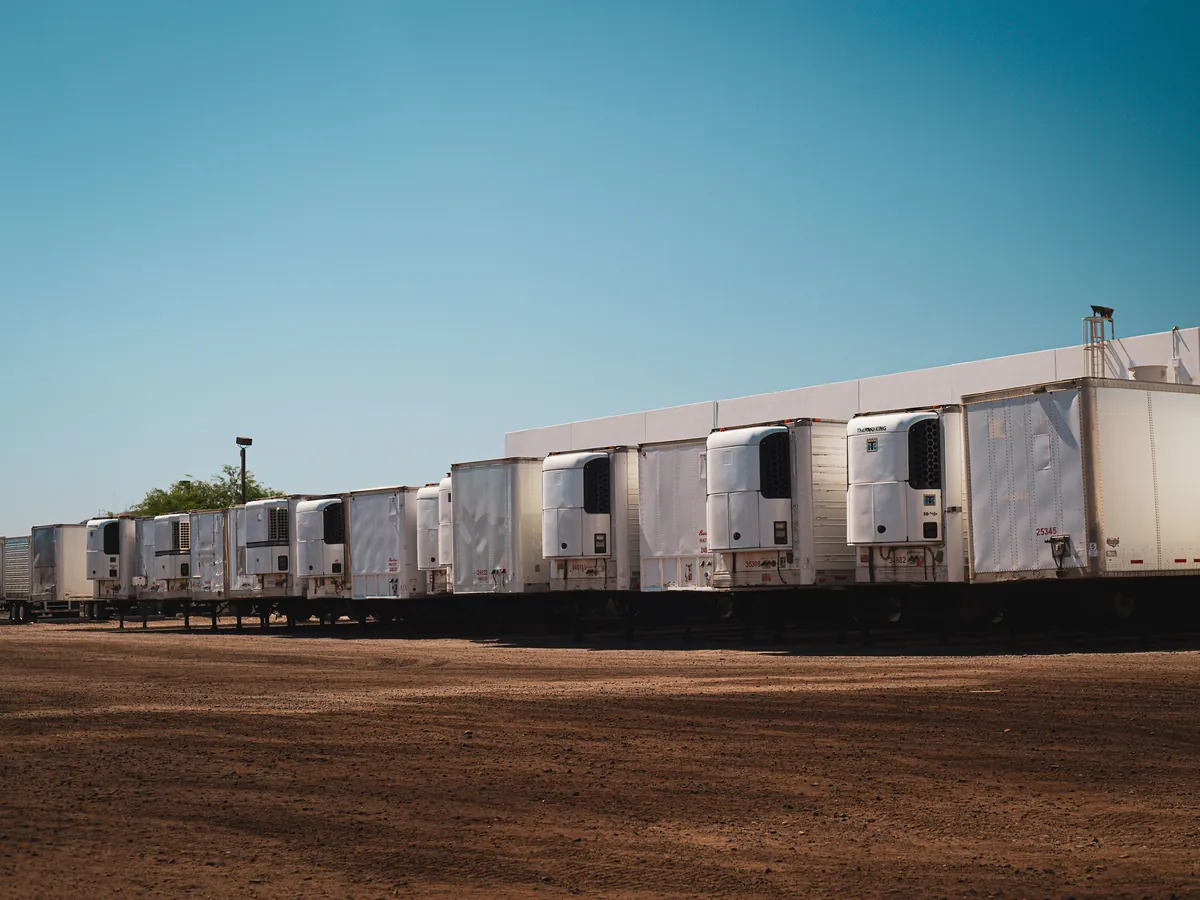A row of refrigerated trailers with cooling units under a clear blue sky.