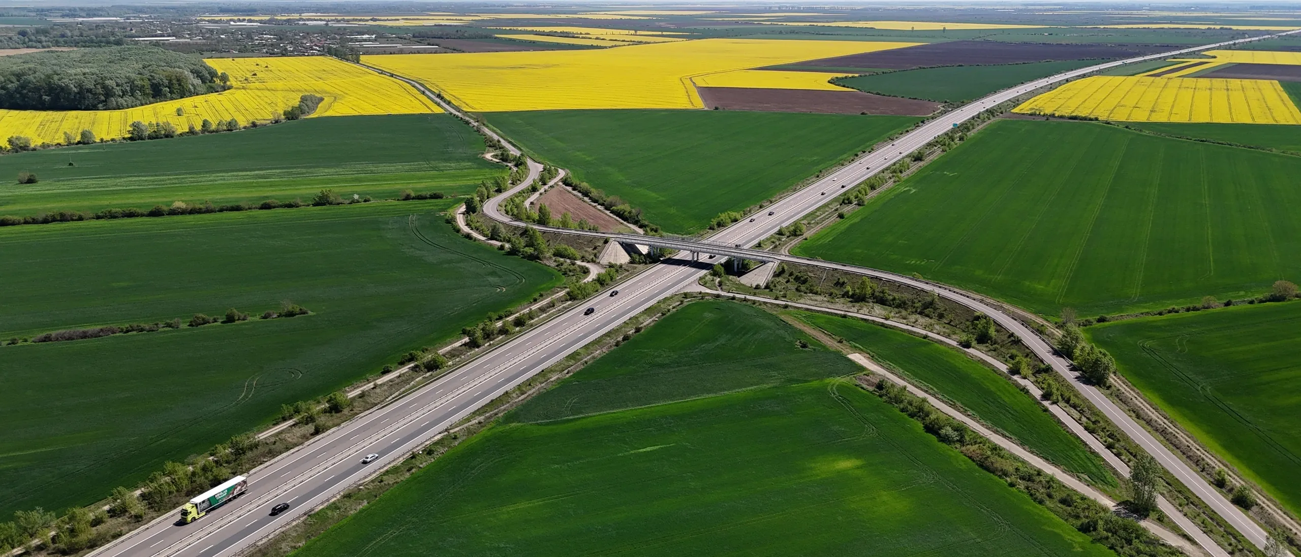 An aerial view of a highway crossing green and yellow farmland in open country.